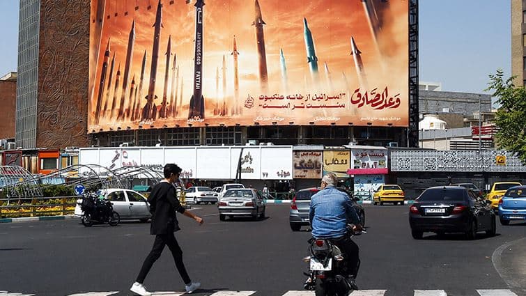 مواطن إيراني يمر أمام لوحة إعلانية لصواريخ بلاده في أحد شوارع طهران - AFP