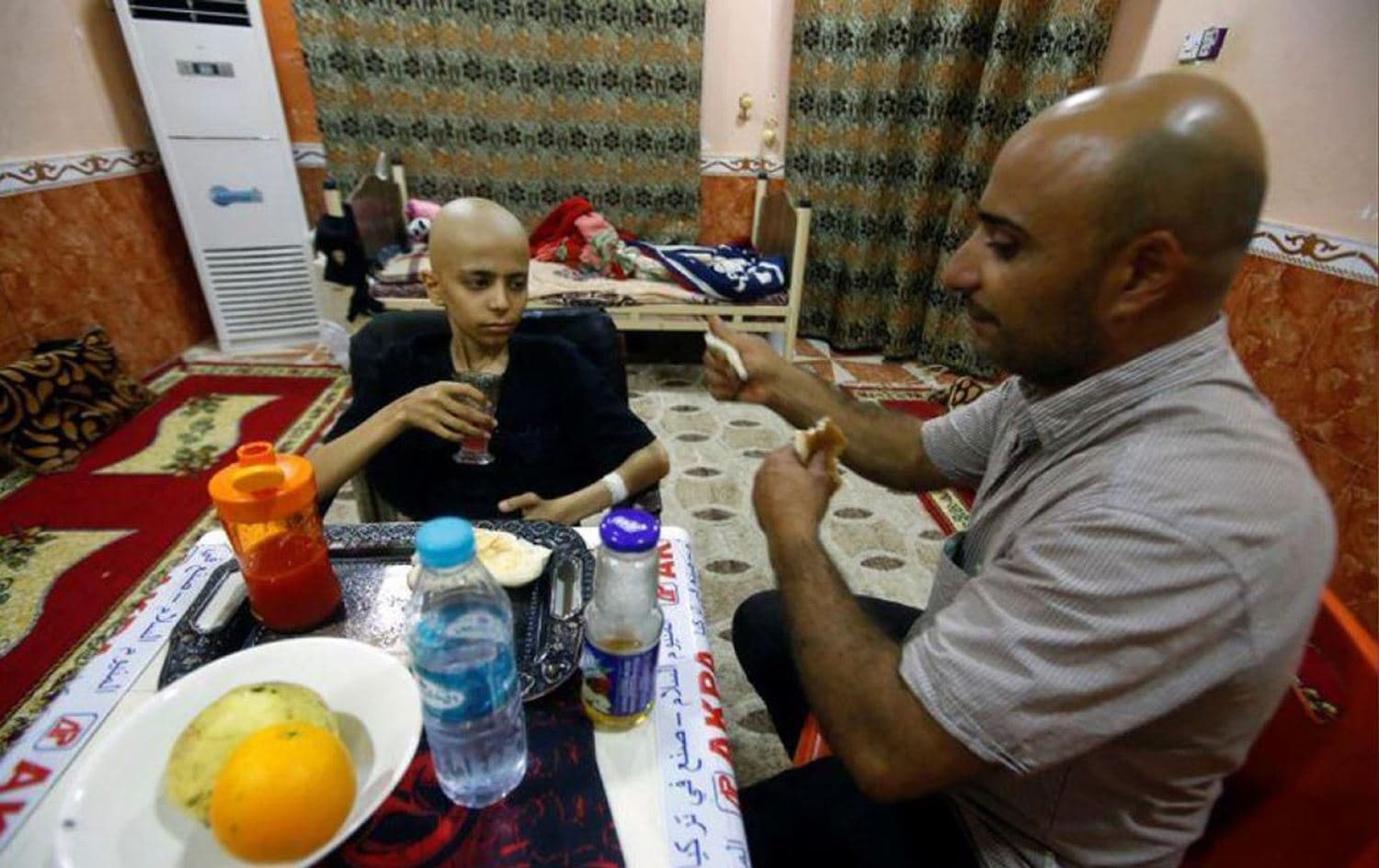 مصطفى عبد الله (14 عاما) المُصاب بالسرطان يتناول الطعام مع والده في منزل عمه في البصرة- رويترز