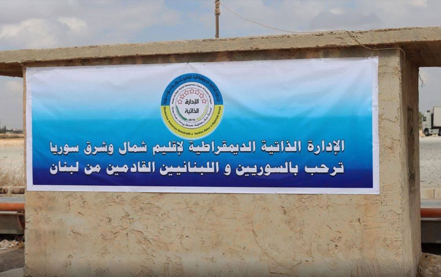 لافتة رُفعت أمام معبر الطبقة الحدودي الذي يفصل مناطق سيطرة الحكومة السورية عن مناطق الإدارة الذاتية لشمال وشرق سوريا